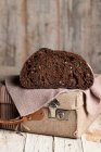 Appetizing healthy dark rye bread loaf with grains cut in half placed on retro fabric suitcase on shabby wooden table — Stock Photo