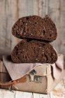 Appetizing healthy dark rye bread loaf with grains cut in half placed on retro fabric suitcase on shabby wooden table — Stock Photo