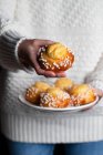 Crop female in white sweater and jeans holding plate with homemade pastry and demonstrating tasty fresh buns with white sprinkles — Stock Photo