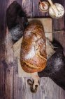 Vista dall'alto appetitosa pagnotta croccante di pane appena sfornato cosparso di farina posta a bordo con tovaglioli su tavolo di legno con ingredienti — Foto stock