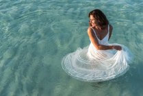 D'en haut dame adulte gaie en robe blanche souriant et dansant dans de l'eau de mer propre — Photo de stock