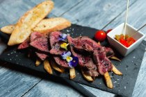 Pieces of yummy beef meat decorated with flowers and placed on french fries near crispy toasts and tasty sauce in cafe — Stock Photo