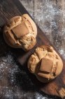 Vista superior de pães de pão fresco colocados em tábua de madeira velha na mesa coberta com farinha na padaria — Fotografia de Stock