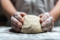 Personne méconnaissable pétrissant la pâte avec de la farine sur la table tout en travaillant dans la boulangerie — Photo de stock