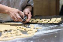 Unrecognizable chef cutting small biscuits from raw dough on metal table covered with flour in bakery — Stock Photo