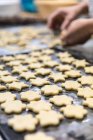 Unbekannter Koch schneidet in Bäckerei kleine Kekse aus rohem Teig auf Metalltisch mit Mehl — Stockfoto