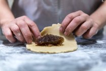Chef méconnaissable rouler la confiture sucrée dans la pâte crue pendant la cuisson de la pâtisserie sur la table dans la boulangerie — Photo de stock