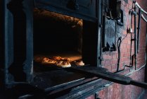 Набір свіжих булочок, поміщених всередину гарячої цегляної печі в професійній пекарні — стокове фото
