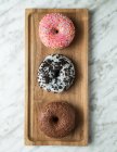 Top view of traditional sweet doughnuts with icing placed on wooden board on light marble surface — Stock Photo