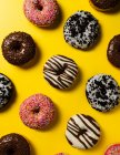 Вид зверху на асортимент смачних солодких глазурованих пончиків, прикрашених глазур'ю та шоколадом та різними видами зморшок на яскраво-жовтому тлі — стокове фото