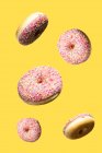 Рожеві солодкі пончики, що плавають на жовтому тлі — стокове фото