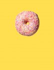 Рожевий солодкий пончик, що плаває на жовтому фоні — стокове фото