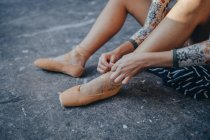 From above side view of crop ballerina sitting on gray floor and putting on pointe while preparing for training in studio — Stock Photo