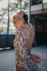 Вид сбоку на молодую грациозную женщину, смотрящую в стильный гимнастический костюм с красочной цветочной печатью и танцующую на открытой спине в балетной студии — стоковое фото