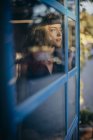 Joven mujer sonriente en traje negro mirando hacia otro lado pensativamente y sonriendo mientras está de pie cerca de la ventana en casa - foto de stock