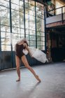 Giovane ballerina drammatica in body nero che esegue una danza sensuale con tulle mentre si allena da sola in uno spazioso studio leggero — Foto stock