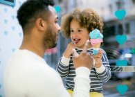 Charmante fille ethnique bouclée tenant cône doux de crème glacée jouer avec père aimant noir dans le café — Photo de stock