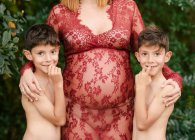 Mujer embarazada abrazando a gemelos en el jardín - foto de stock