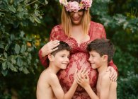 Mujer embarazada abrazando a gemelos en el jardín - foto de stock