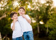 Glückliche Zwillingsjungs umarmen sich und schauen in die Kamera im Park — Stockfoto
