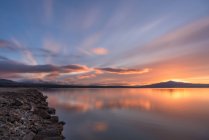Lange Belichtung malerischer Blick auf bewölkten Sonnenuntergangshimmel über Berg und friedliches Seewasser in der Natur — Stockfoto