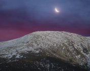 Ampla vista de ângulo de tirar o fôlego da gama de montanhas nevadas contra o céu noturno com nuvens brancas e lua na natureza — Fotografia de Stock