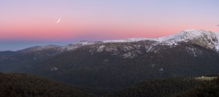 Дивовижний широкий кут зору сніжного гірського хребта на вечірнє небо з білими хмарами і місяцем в природі — стокове фото