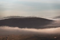Moinhos de vento da estação eólica moderna localizada na colina na manhã enevoada no campo — Fotografia de Stock