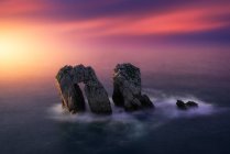 Desde arriba de rocas ásperas entre el mar azul tranquilo bajo el colorido atardecer cielo nublado - foto de stock