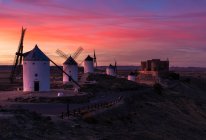 Antichi mulini a vento e castello invecchiato contro il luminoso cielo del tramonto in campagna — Foto stock