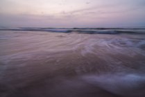 Meereswellen rollen an nasser Sandküste gegen wolkenverhangenen Himmel am Abend in der Natur — Stockfoto