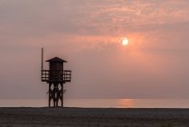 Деревянная башня-спасатель, расположенная на песчаном берегу против закатного неба на курорте — стоковое фото