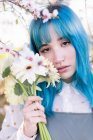 Moderna donna alla moda con i capelli blu in possesso di bouquet di fiori freschi e guardando la fotocamera mentre in piedi in giardino fiorito primavera — Foto stock