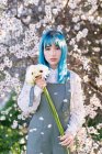 Moderna donna alla moda con i capelli blu in possesso di bouquet di fiori freschi e guardando la fotocamera mentre in piedi in giardino fiorito primavera — Foto stock