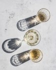 Вид зверху композиція різних окулярів з алкогольними напоями на сонячному світлі залишає тіні і світло на мармуровій поверхні — стокове фото