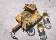 Top view composition with glasses of wine served with sliced cheese and bread with jam on marble table with wooden board in sunlight — Stock Photo