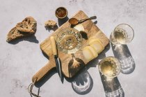 Composición vista superior con copas de vino servidas con queso en rodajas y pan con mermelada sobre mesa de mármol con tabla de madera a la luz del sol - foto de stock