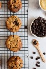 Vista superior de deliciosos biscoitos caseiros recém-assados com chips de chocolate colocados na grade da cozinha perto de tigelas com ingredientes — Fotografia de Stock