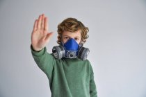 Blond boy, wearing a respirator and showing stop sign — Stock Photo