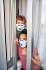 Madre e hijo mirando por la ventana de su casa para ver si el peligro de una posible infección ha pasado - foto de stock
