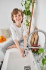 Criança loira lavando as mãos na pia da cozinha para evitar qualquer infecção — Fotografia de Stock