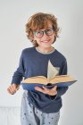 Blond kid in pajamas with a book playing research — Stock Photo