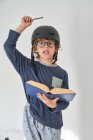 Blond kid in pajamas with a helmet and a book playing research — Stock Photo