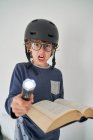 Blond kid in pajamas with a helmet a flashlight and a book playing research — Stock Photo