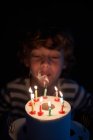 Rubio chico soplando las velas en su papel higiénico pastel de cumpleaños - foto de stock