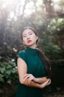 Молода азіатка в модному одязі в зелених кущах і дивиться на камеру в літньому саду — стокове фото