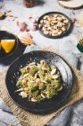 Сверху часть вкусной жареной зеленой брокколи с миндалем на черной тарелке на сером столе в композиции с различными ингредиентами для приготовления блюд в домашних условиях — стоковое фото