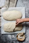 From above top view cropped unrecognizable person hand cutting artisan bread loaf in a table dusted with white flour — Stock Photo