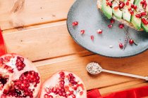 Top view of halved pomegranate and spoon with seeds placed near plate with delicious avocado toast on wooden table — Stock Photo