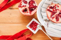 Top view of red ribbon placed on lumber table near plate with halves of ripe pomegranate and spoon — Stock Photo